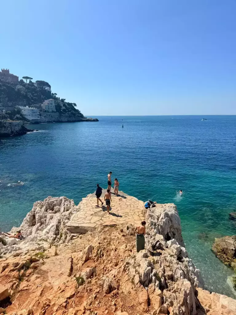 Baigneurs sur les rochers du littoral de Nice face à une mer turquoise.